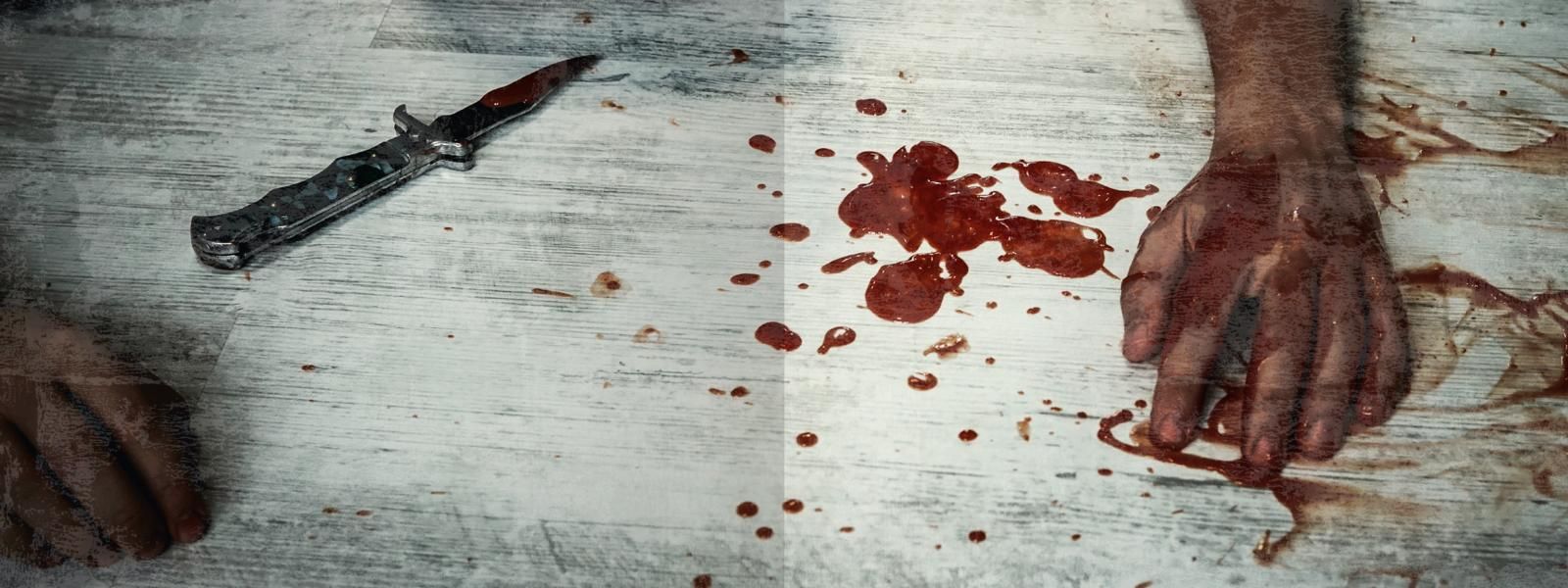 Gezeigt wird eine Innen- oder Zusatzansicht von „Escape Room. Das Geheimnis des Spielzeugmachers“. Die Szene zeigt einen Holzuntergrund mit blutigen Flecken und einem kleinen Messer. Zwei Hände sind sichtbar, eine davon mit Blut beschmiert. Die Farbgebung