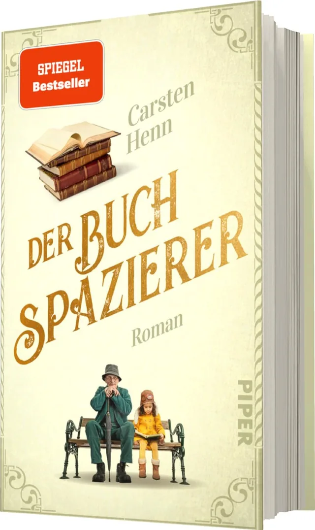 Das Buchcover zeigt einen sanften, hellen Hintergrund mit goldenen und braunen Schriftzügen. Im Zentrum steht der Titel „DER BUCHSPAIZIERER“ in großer, geschwungener Schrift. Darunter ist der Autorennamen „Carsten Henn“ und die Bezeichnung „Roman“ in schl