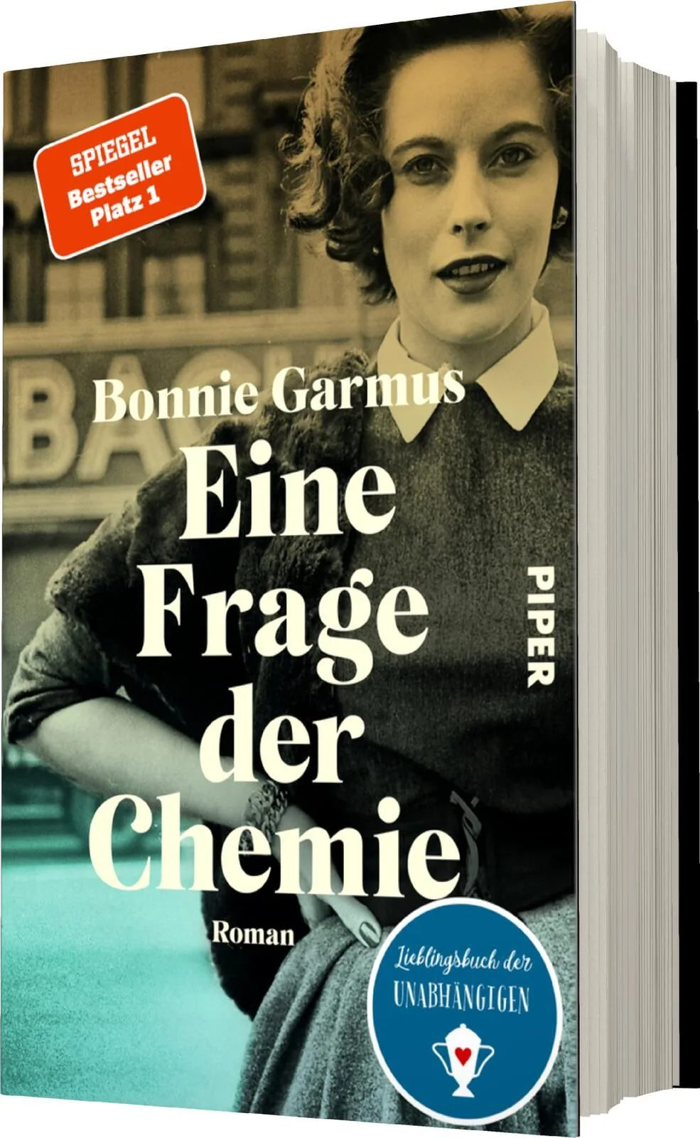 Das Buchcover zeigt eine schwarz-weiß gehaltene Portraitaufnahme einer Frau mit lockigem Haar, die in einem modernen, eleganten Kleid erscheint. Ihr Blick ist selbstbewusst, und sie steht vor einem urbanen Hintergrund. Der Titel „Eine Frage der Chemie“ is