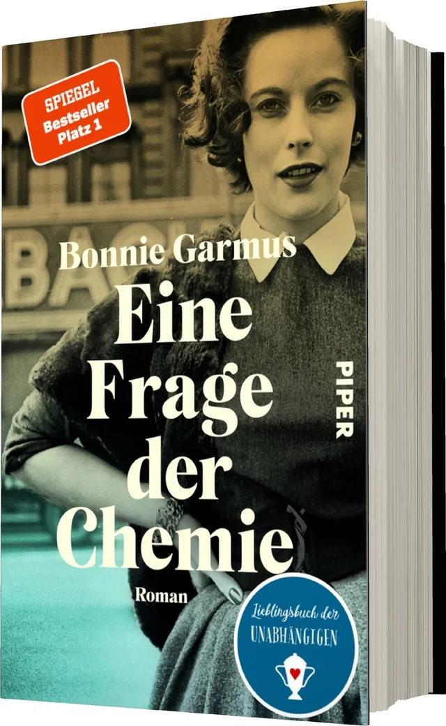 Das Buchcover zeigt eine schwarz-weiß gehaltene Portraitaufnahme einer Frau mit lockigem Haar, die in einem modernen, eleganten Kleid erscheint. Ihr Blick ist selbstbewusst, und sie steht vor einem urbanen Hintergrund. Der Titel „Eine Frage der Chemie“ is