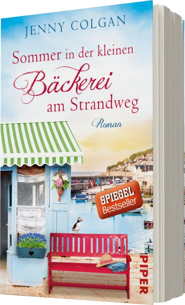 Das Buchcover zeigt eine charmante Bäckerei am Strandweg, umgeben von einem malerischen Hafen. Die Hütte hat ein grün-weiß gestreiftes Dach und ist geschmückt mit Blumen. Im Vordergrund steht eine rote Bank, auf der eine Strandtasche liegt. Der Himmel ist