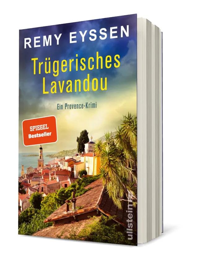 Cover von „Trügerisches Lavandou“ von Remy Eyssen: Eine malerische Küstenlandschaft mit einem Dorf, umgeben von Bäumen und Hügeln, in warmen Farbnuancen und einer mysteriösen Stimmung.